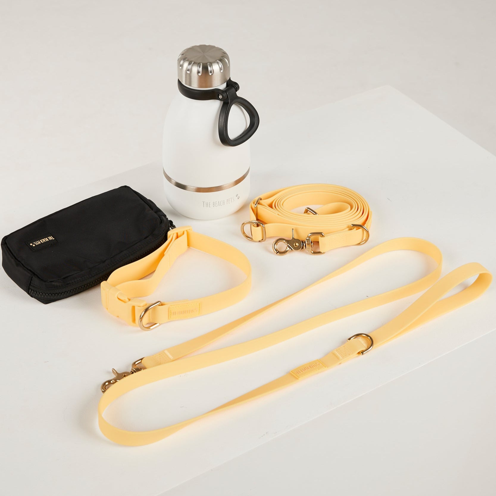 Black pouch, white water bottle with black handle, and yellow dog leashes on a light gray background