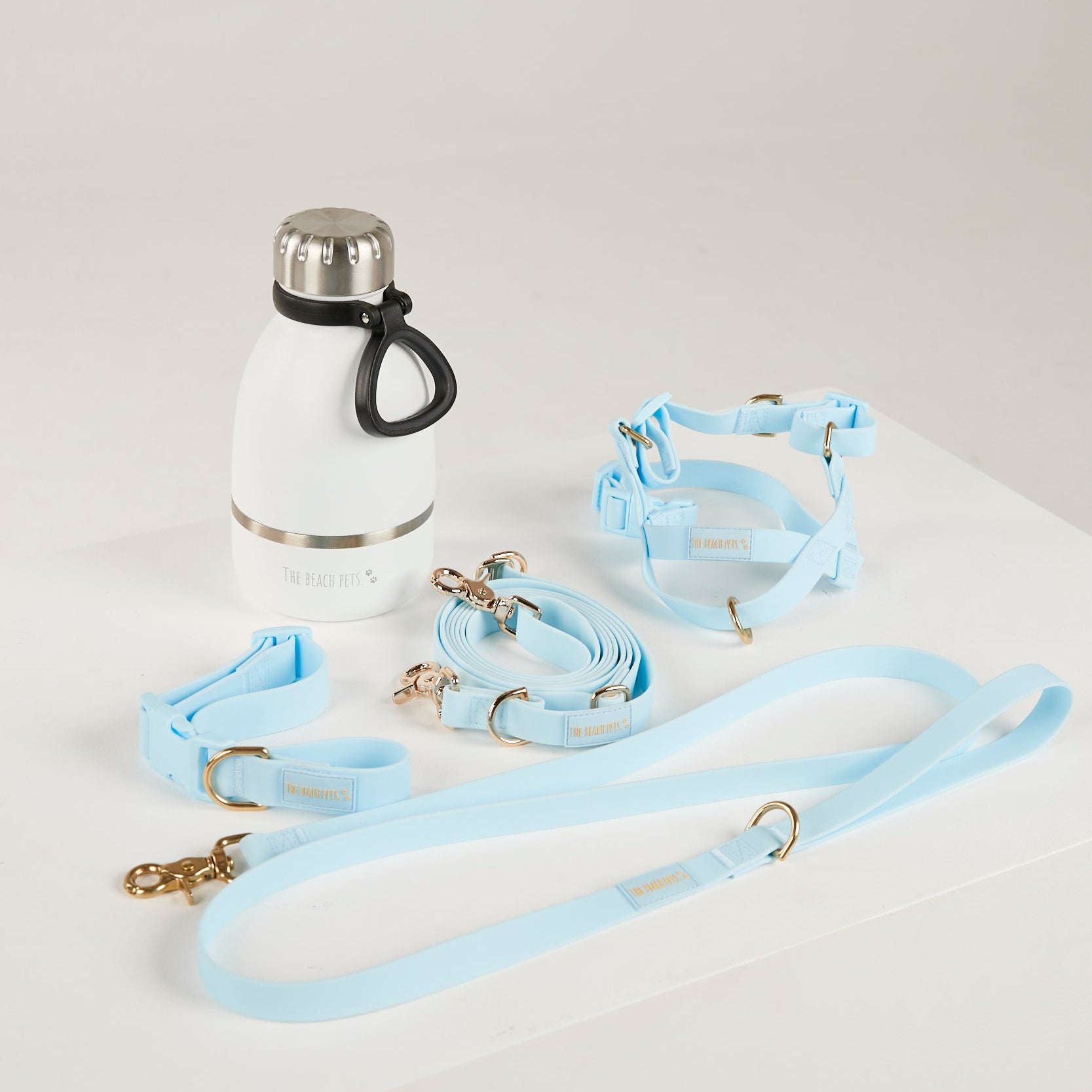 Light blue dog collar, leash, and harness set with a white water bottle on a light gray background