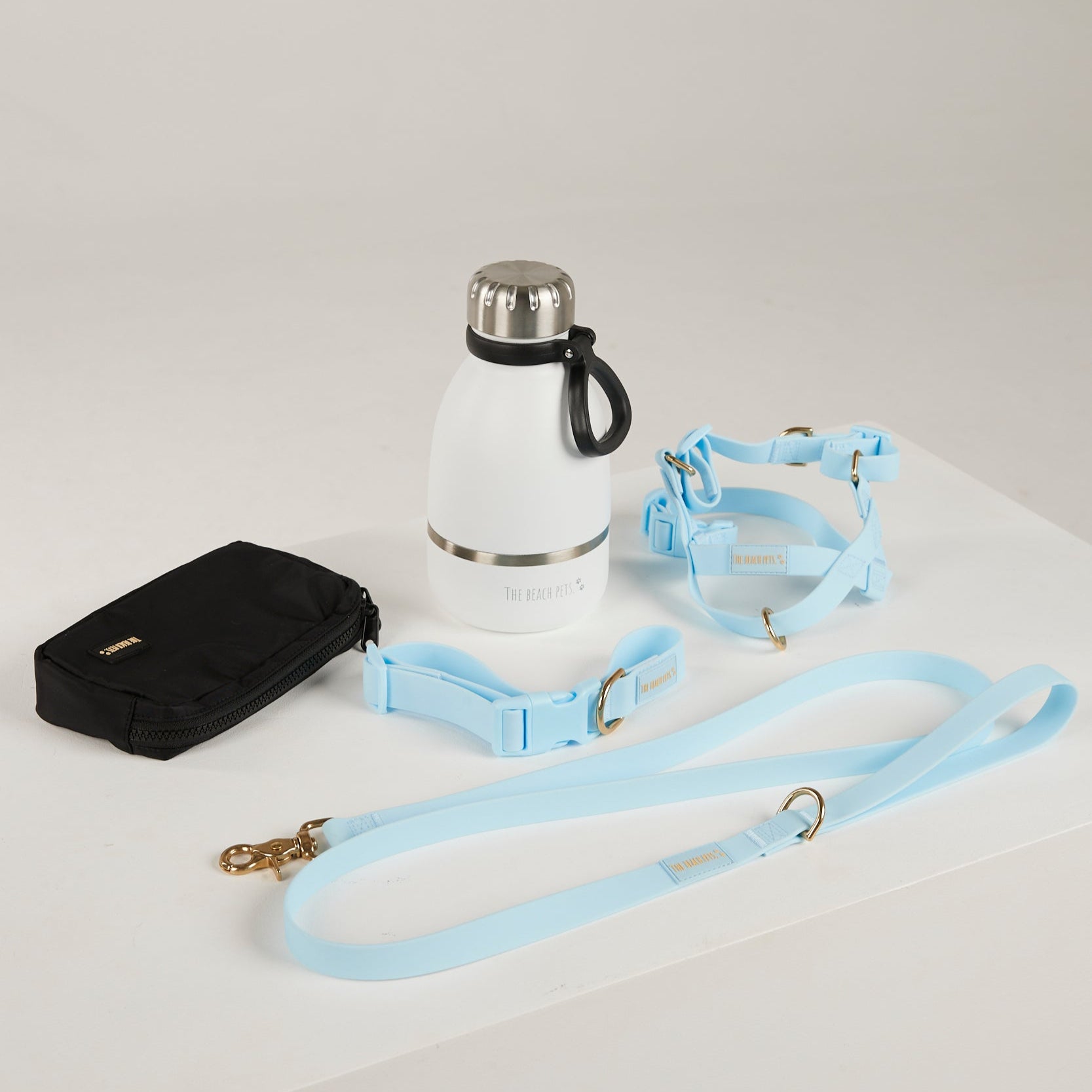 White thermos with black handle, black pouch, and light blue dog leashes on a white background