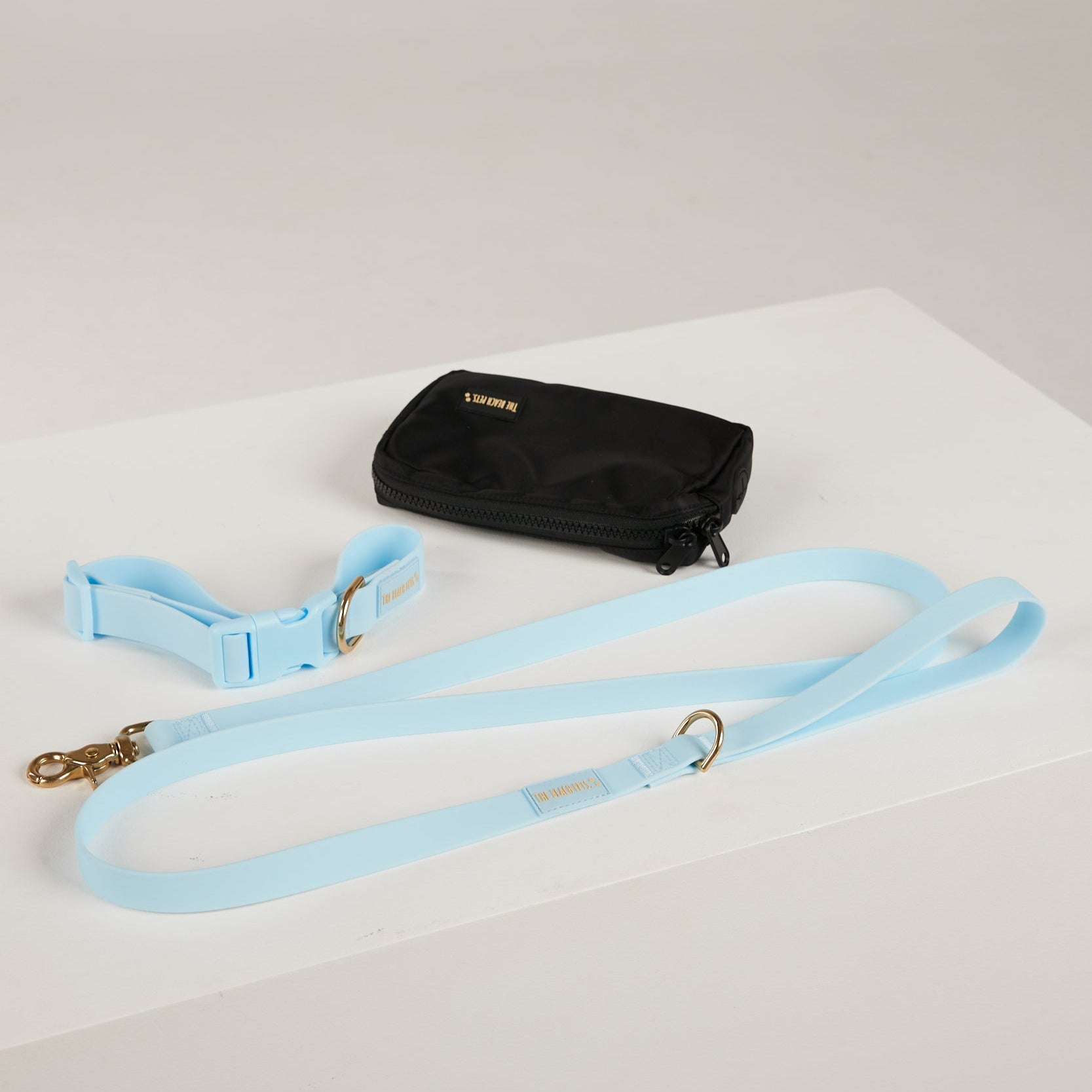 Black pouch and light blue dog leash on a white surface