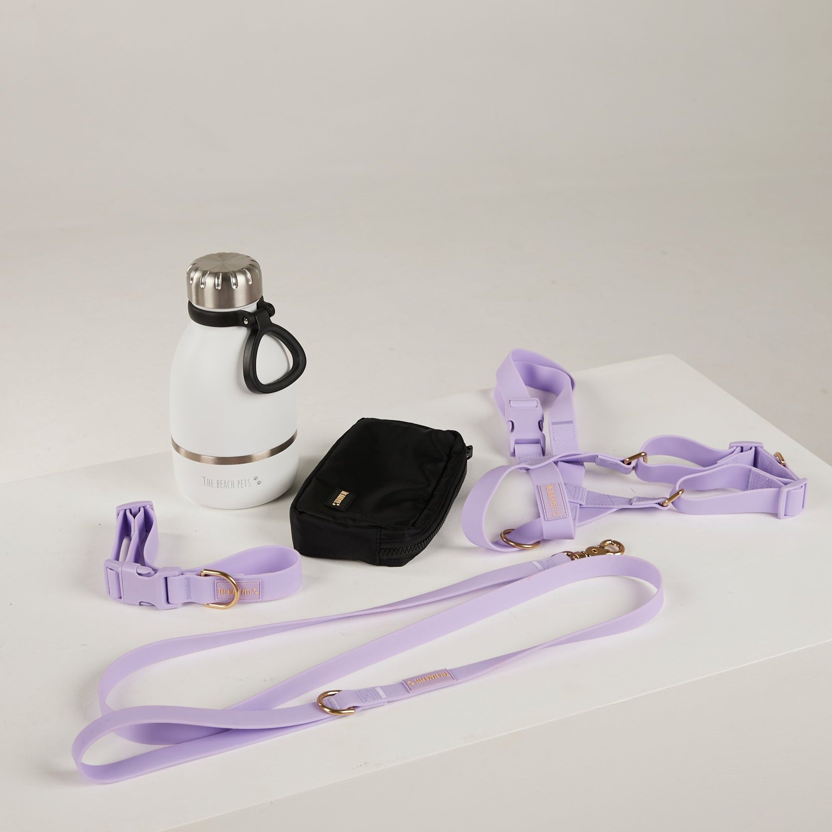 Lavender dog collar, leash, and harness on a white surface with a white water bottle.