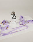 Lavender dog collar, leash, and bottle on a white surface with a light gray background