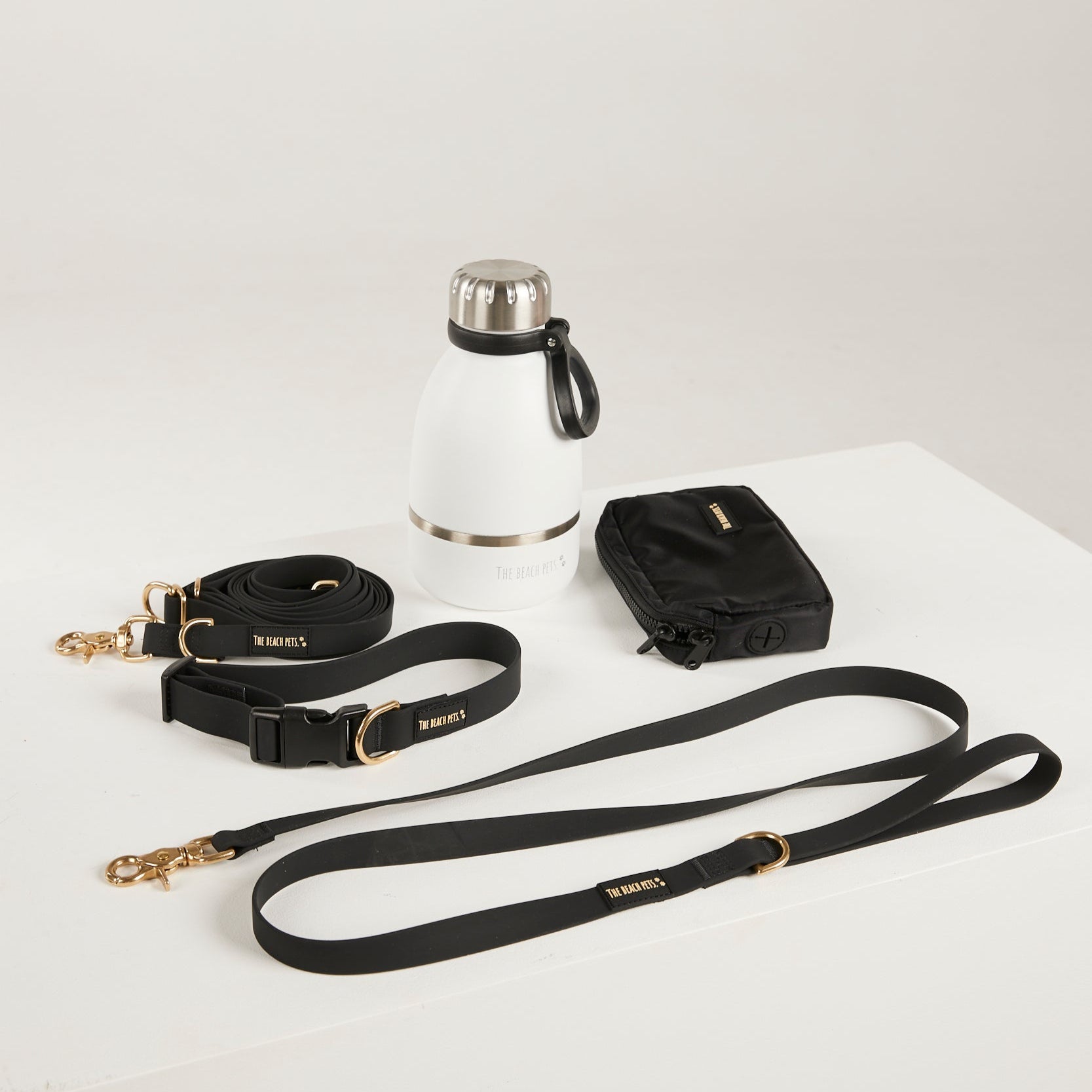 Black dog leash and collar set with a white water bottle on a light gray background