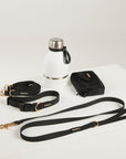 Black dog leash and collar set with a white water bottle on a light gray background