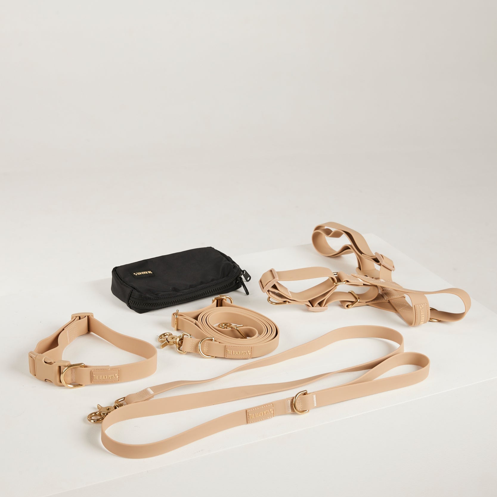 Dog training equipment including a black bag, beige leashes, and a collar on a light gray background.