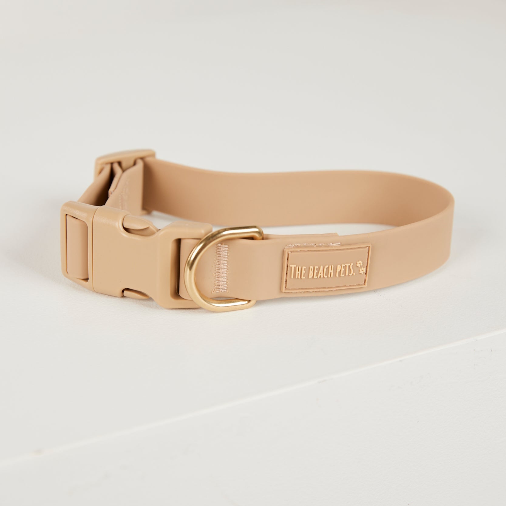 Beige dog collar with a gold buckle on a light gray background
