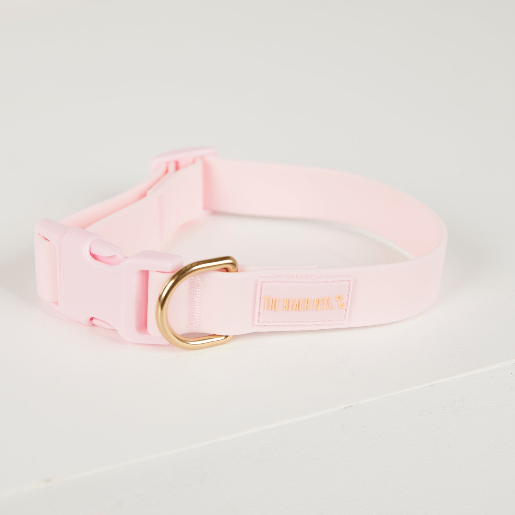 Pink dog collar with a gold buckle on a light gray background