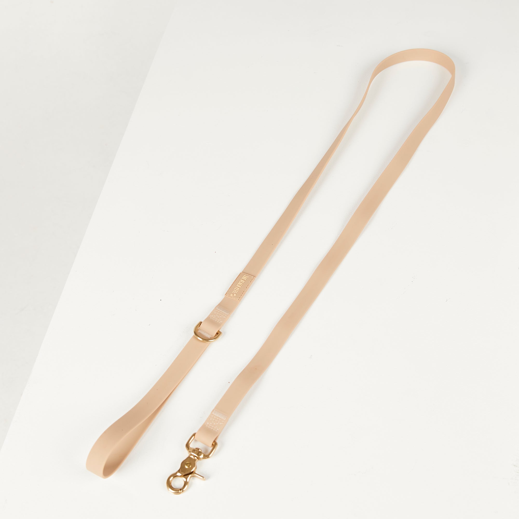 Beige dog lead with a gold clasp on a light gray background