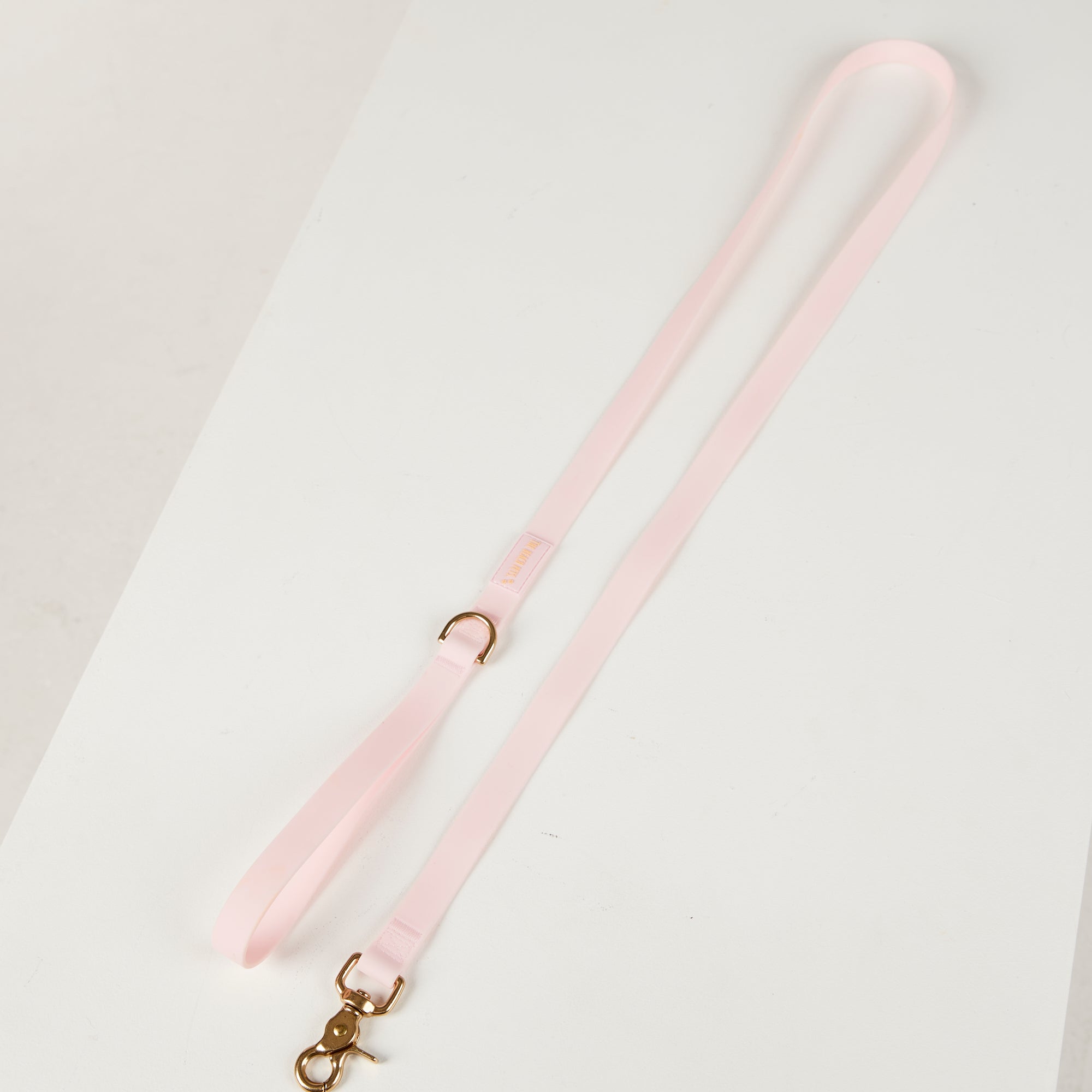 Pink dog lead with a gold clasp on a light gray background