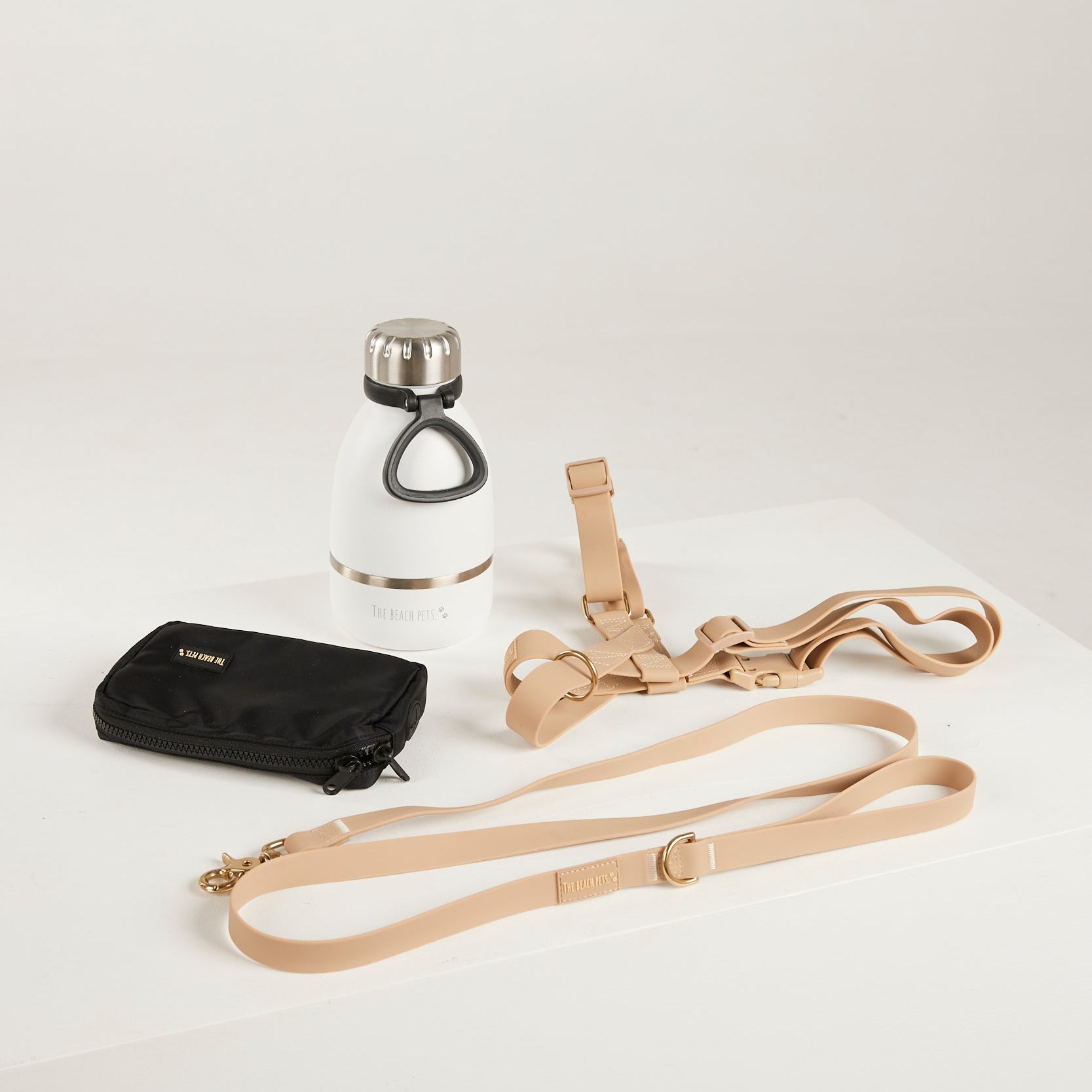 Black pouch, white water bottle with silver cap, and beige dog leashes on a light gray background