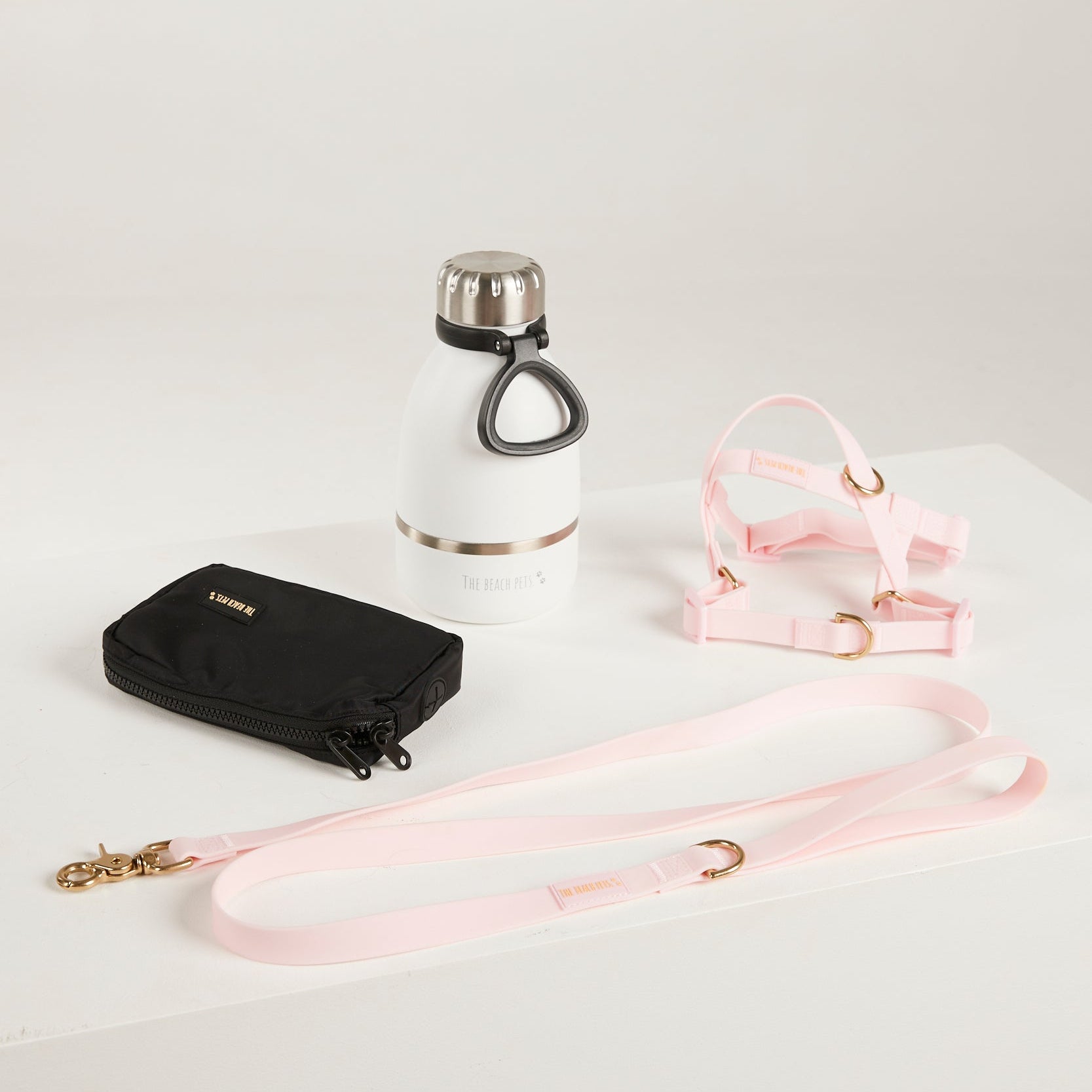 White water bottle with black cap, black wallet, and pink leash on a light gray background